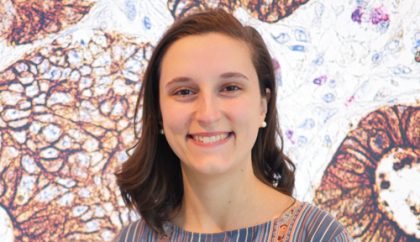 Person with long, brown hair stands in front of image of cells