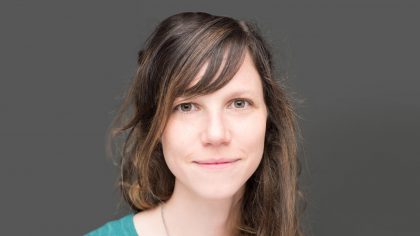 Person with shoulder-length hair in front of a grey background.