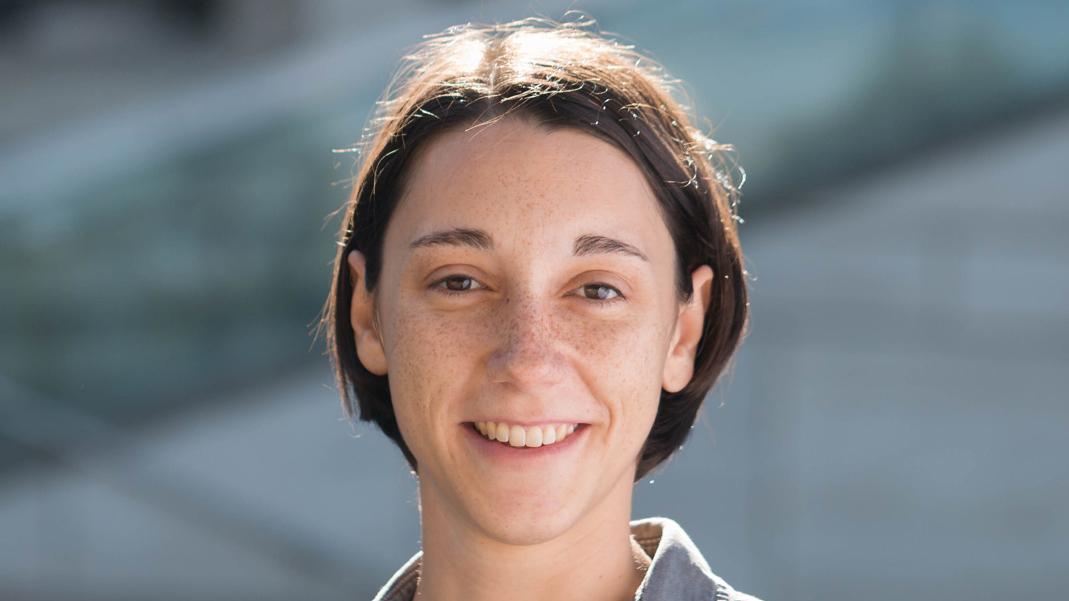 Person with short hair outdoors in front of blue background.
