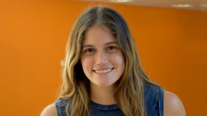 Person with shoulder-length hair in front of an orange backdrop.