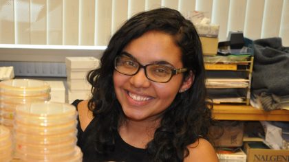 Person with long, curly hair and glasses smiling in an office setting.