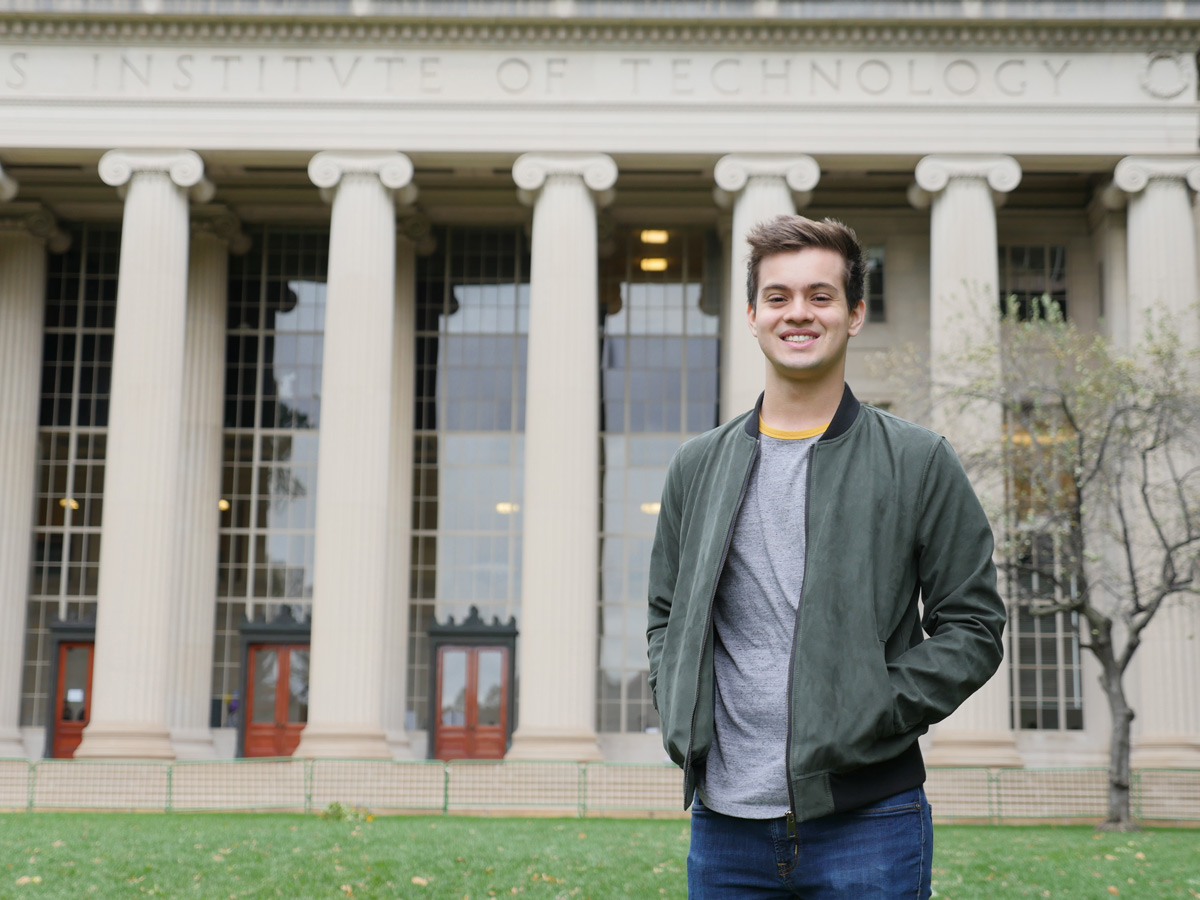 Person with short brown hair and green jacket stands in front of MIT pillars.