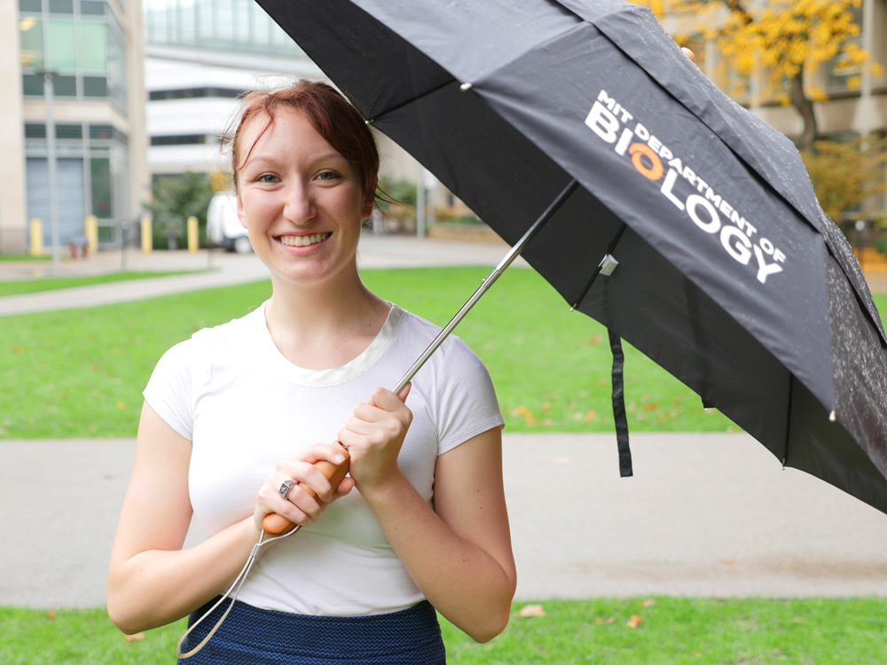 Person with red hair in bun stands outside with umbrella.
