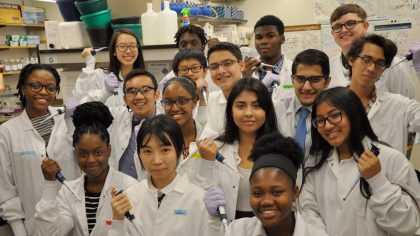 Group of happy female and male students in lab coats holding lab equipment