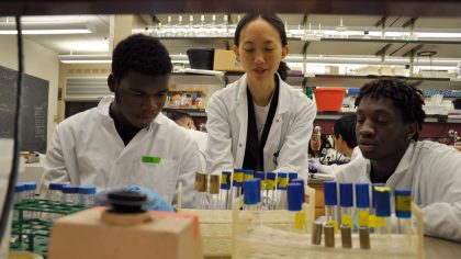 Three students in lab coats looking at test tubes