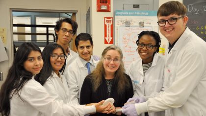 Six students in lab coats and a professor in the middle in black