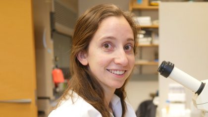 Person with long, brown hair smiling at microscope