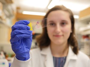 Person with long, brown hair and lab coat looks at slide