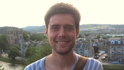 Person with short, brown hair in front of landscape