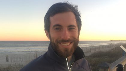 Person with dark hair and beard on sea coast.