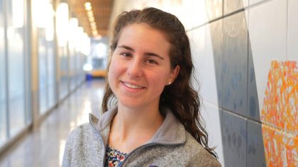 Person with long, brown hair smiling in hallway