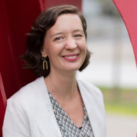 Woman with short hair smiling outside by red statue