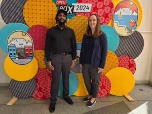 two people smiling, standing in front of a colorful wall. 