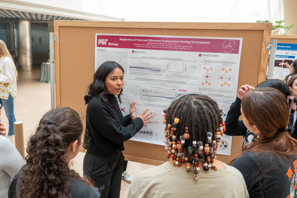 Mariely Morales Burgos standing in front of a paper poster, indicating a certain point of data to three people
